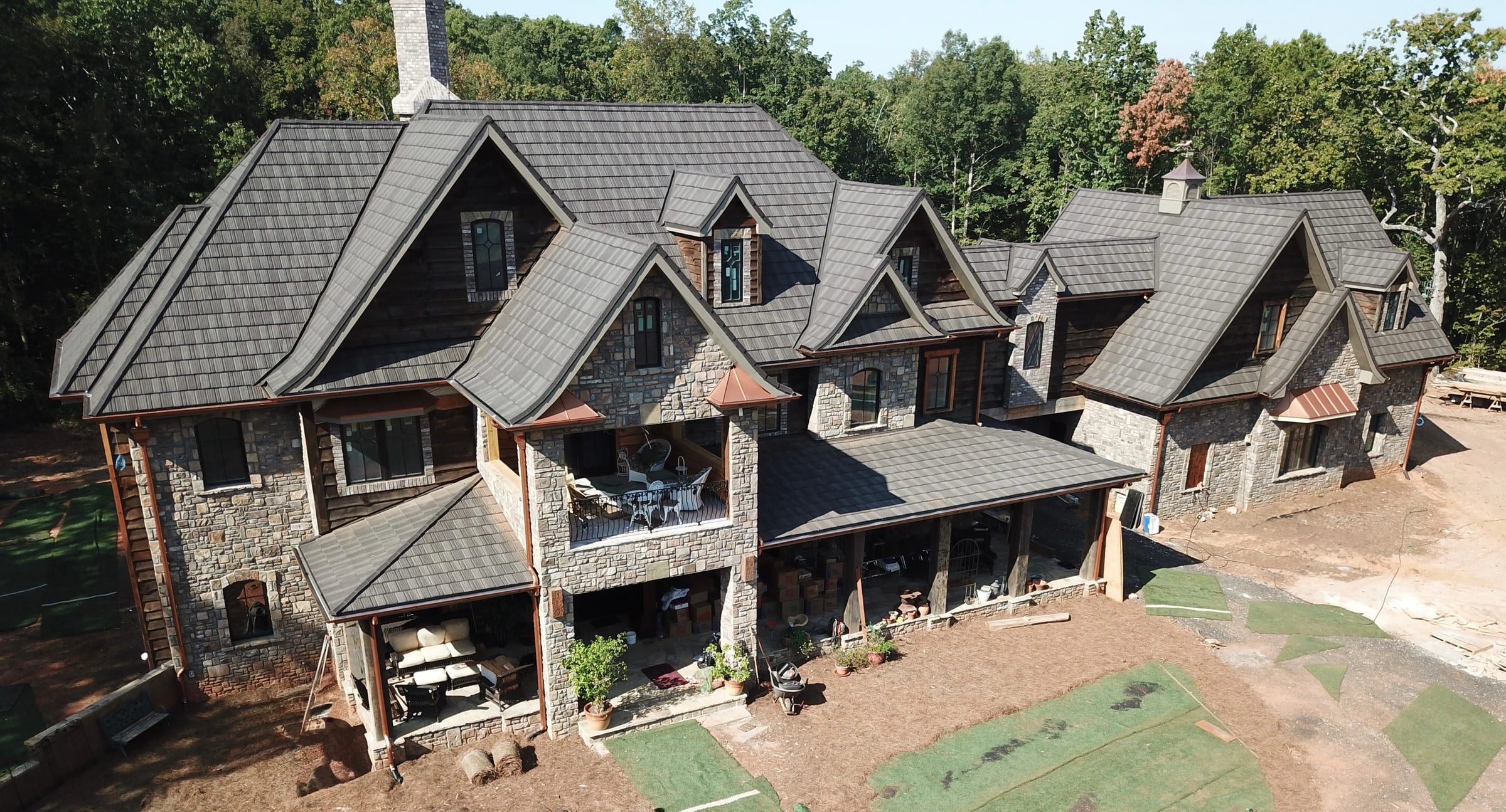 Aerial view of a gray stone-coated steel shake roof on a large stone and timber home with many gables