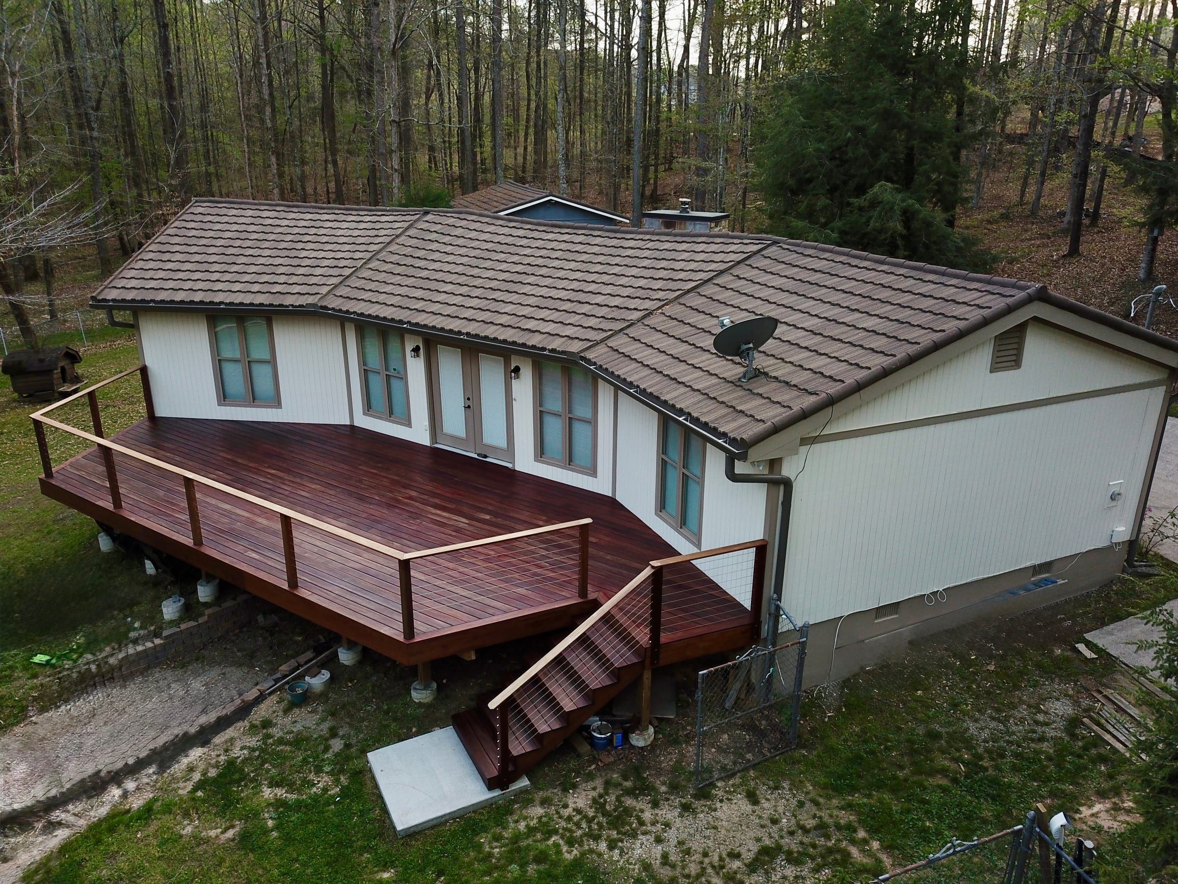 Aerial view of a brown stone-coated steel tile roof and a new hardwood deck with cable railings