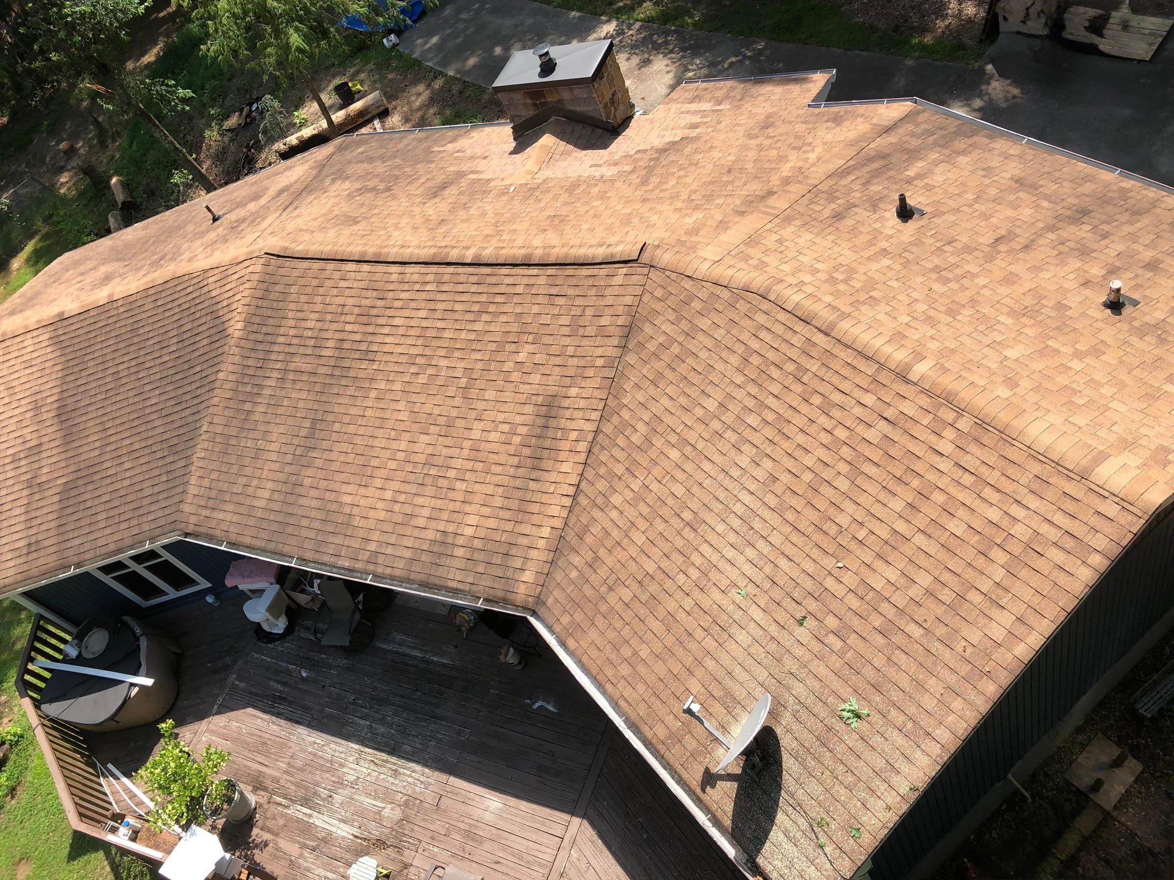 Aerial view of a faded, worn asphalt shingle roof and a weathered wood deck before replacement